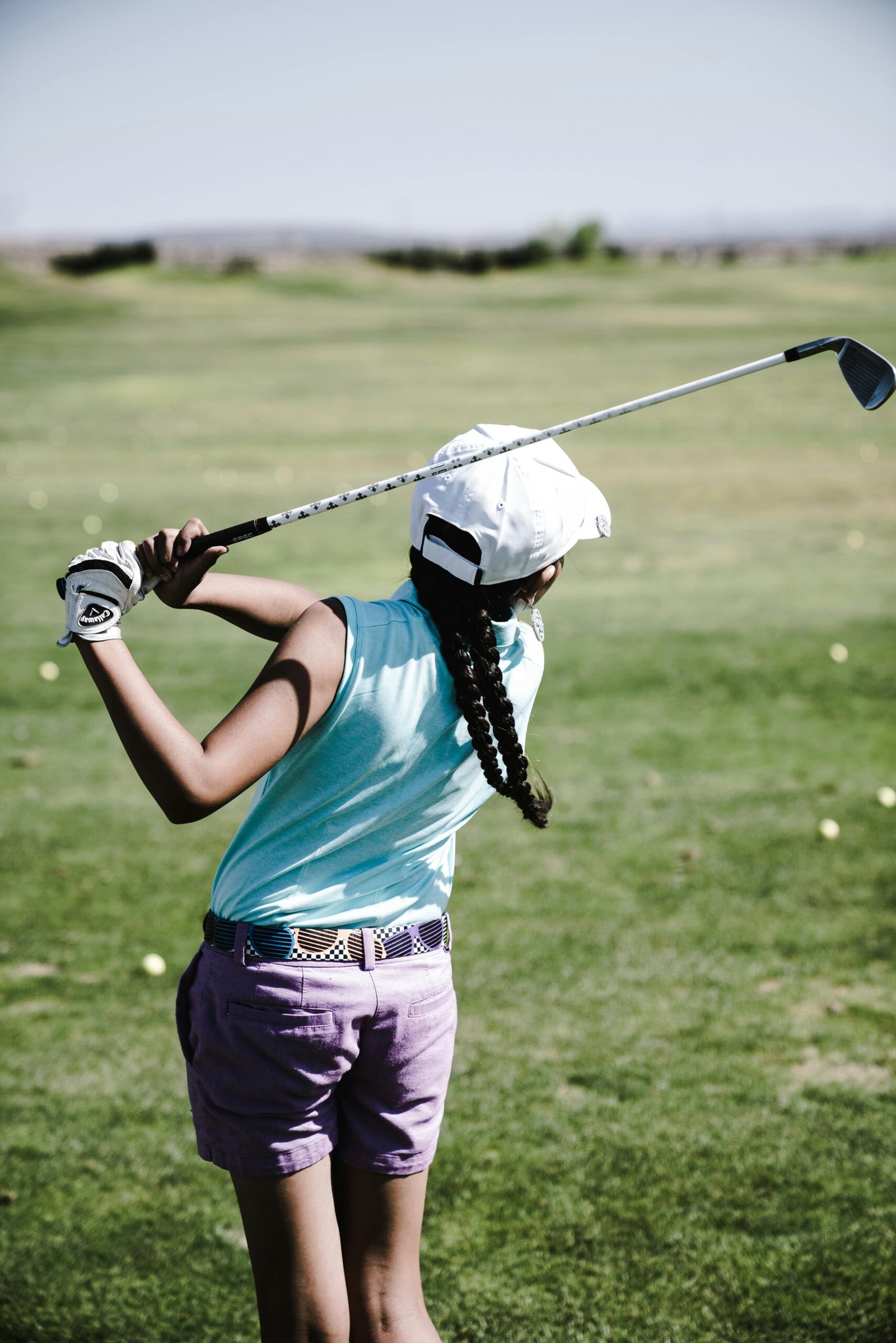 "Girl playing golf on a sunny course, holding a club and preparing for a swing, with boxes of golf equipment visible in the foreground."